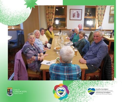 Grŵp o bobl oedrannus yn eistedd wrth fwrdd yn cael bwyd